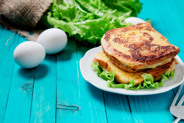 
sandwich with cheese and mayonnaise fried in egg with lettuce on a wooden background