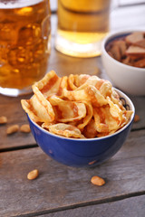 Mugs of beer and bowls with snacks on wooden table