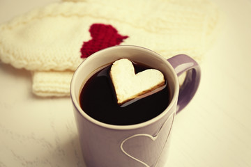 Cup of hot coffee with heart marshmallow and warm mittens on light wooden background, close up