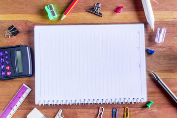 High Angle View of Colorful School Supplies Organized by Type Around Note Book Open to Blank Page...