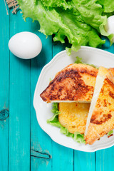 
sandwich with cheese and mayonnaise fried in egg with lettuce on a wooden background