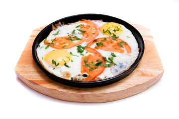 fried eggs with tomatoes in a frying pan on a wooden stand