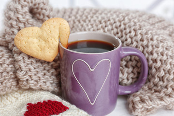 Heart shape cookie on cup of coffee with knitted cloth closeup