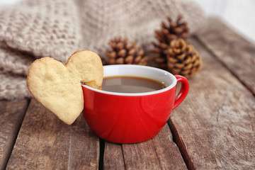 Heart shape cookie on cup of coffee on wooden table closeup