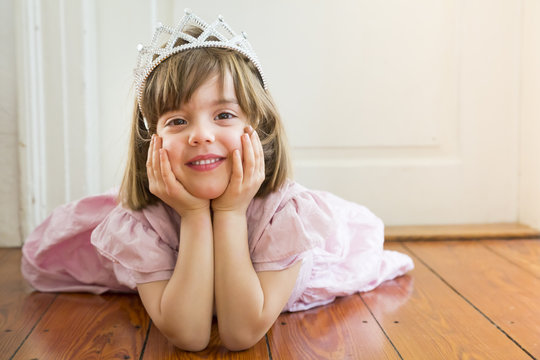 Portrait of smiling little girl dressed up as a princess lying on wooden floor