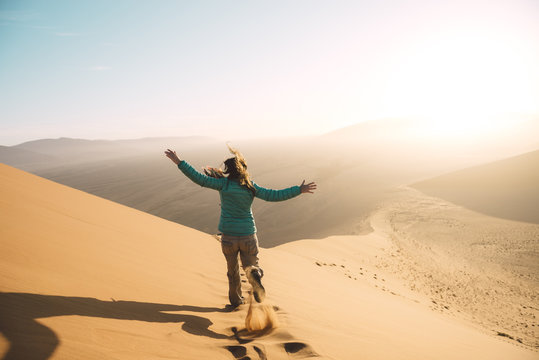 Namibia, Namib Desert, Sossusvlei, Woman running down the Dune at sunrise