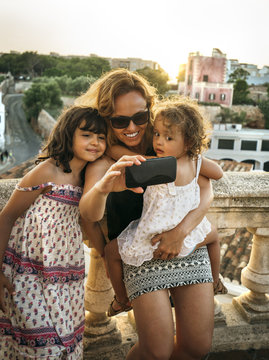Spain, Menorca, woman and her little daughters taking a selfie with smartphone