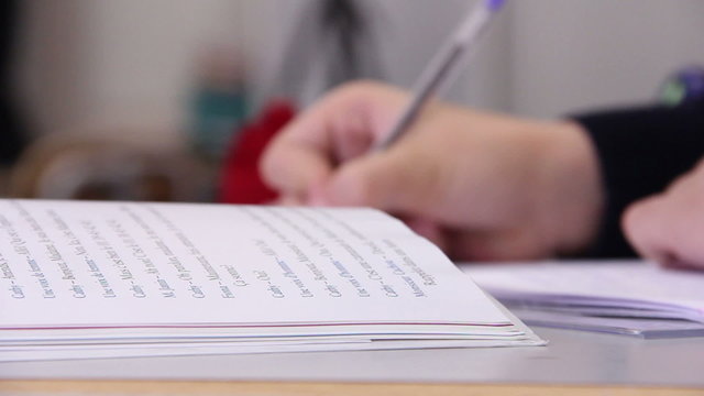 An open textbook with a hand writing notes in focus. Focus pull to the text book. 