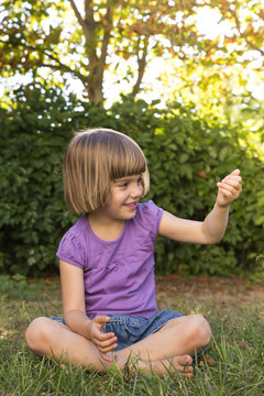 Smiling little girl sitting on a meadow watching something in her hand
