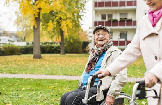 Senior woman with wheeled walker and senior man in wheelchair outdoors in autumn