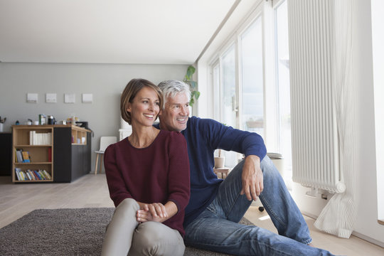 Smiling couple sitting on the floor at home watching something