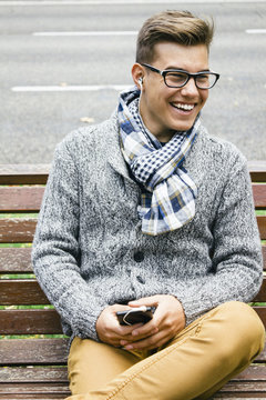 Portrait of smiling teenage boy sitting on a bench hearing music with earphones