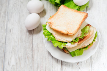 
sandwich with chicken breast , egg, lettuce, cheese and mayonnaise on a wooden background