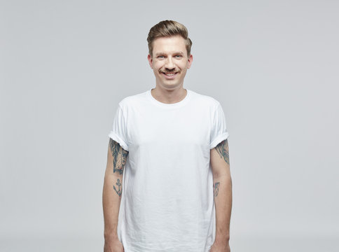 Portrait of smiling man with tattoos on his arms wearing white t- shirt in front of grey background