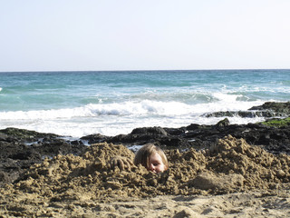 Spain, Canary Islands, Fuerteventura, boy at the sea buried in sand