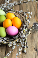 Easter background, selective focus. Homemade hand painted colorful easter eggs in nest from willow branches close-up over retro wooden rustic background