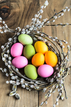 Easter background, selective focus. Homemade hand painted colorful easter eggs in nest from willow branches close-up over retro wooden rustic background