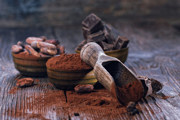 Dark chocolate pieces, cocoa powder and cocoa beans on a wooden table
