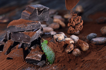 Dark chocolate pieces, cocoa powder and cocoa beans on a wooden table