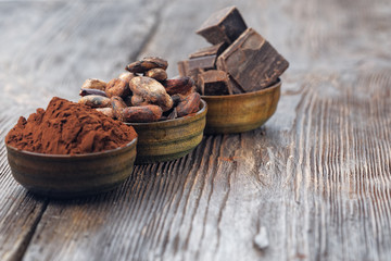 Dark chocolate pieces, cocoa powder and cocoa beans on a wooden table