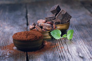 Dark chocolate pieces, cocoa powder and cocoa beans on a wooden table