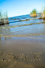 The seashore, waves. On the beach, the sand is written the word "sale".