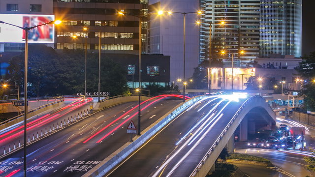 Hong Kong Business District timelapse at Night. Corporate building at the back and busy traffic across the main road at rush hour.
