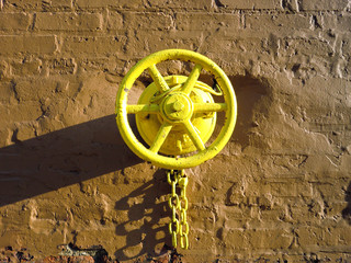 Centered yellow industrial valve wheel with chain on brick wall- landscape color photo