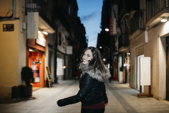Spain, Reus, portrait of smiling young woman walking at pedestrian area in the evening
