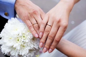 Man and woman hands with wedding rings, bride's bouquet in background