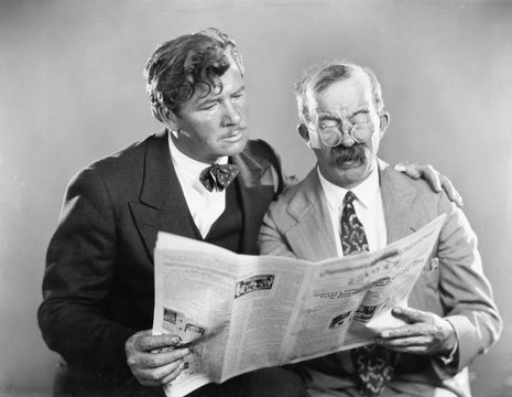 Two mature men reading a newspaper together 