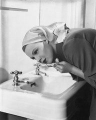Woman washing face over sink 