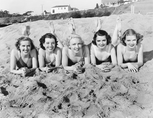 Portrait of five young women lying on the beach and smiling 