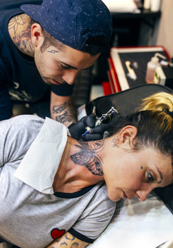 Woman receiving butterfly tattoo at her neck