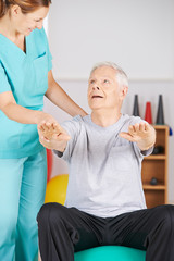 Obraz premium Senior auf Gymnastikball bei der Physiotherapie