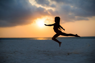 Fototapeta na wymiar Silhouette of adorable little girl on white beach at sunset