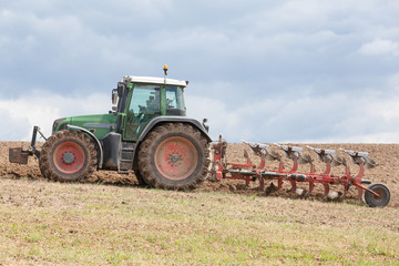 Farmer ploughing, or plowing,  a field preparing the soil for the planting of the spring crop with a tractor and plough