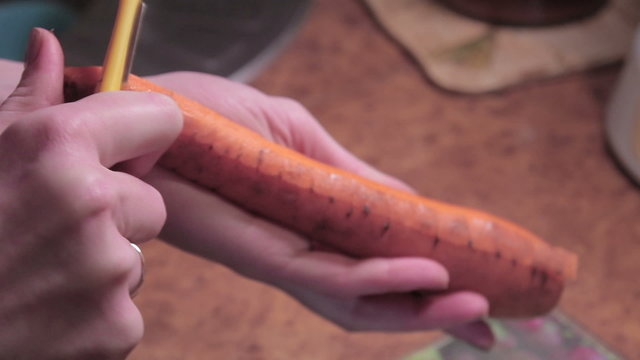 Girl in jamper cleaning carrot, knife
