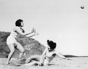Two women playing with a ball at the beach  - obrazy, fototapety, plakaty