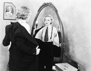 Young woman in men's clothing getting undressed in front of a mirror 