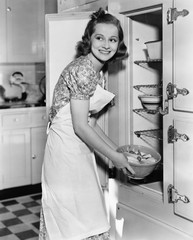 Young woman in an apron in her kitchen taking food out of the refrigerator 