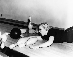 Woman sliding down bowling alley with ball 