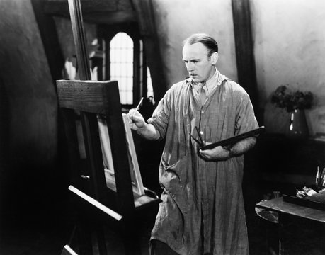 Man painting on an easel with a paintbrush 