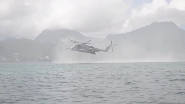 Navy Seals train on rubber zodiac watercraft while a helicopter performs a helicasting maneuver. 