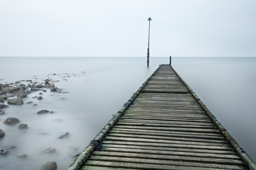 Fototapeta premium Long abandoned rotted jetty leading out to sea on a cold misty afternoon in Llandudno, Wales, UK.