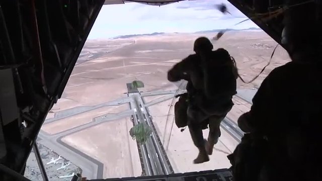 Paratroopers jump from an airplane over an airfield.