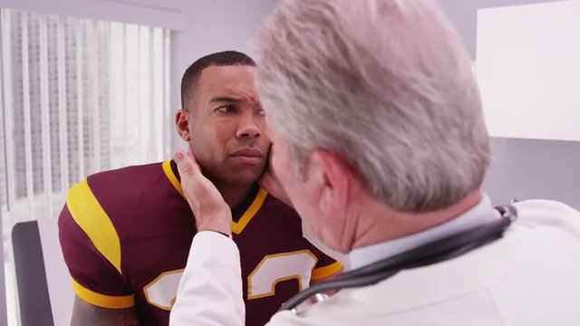 College football player having senior doctor review his concussion injury