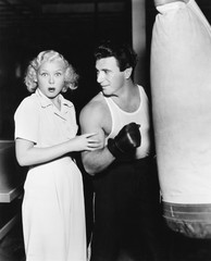 Woman standing next to a boxer feeling his arms and being astonished 