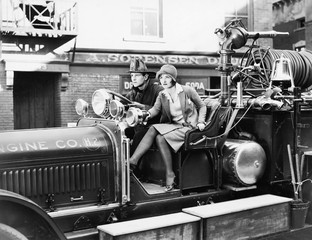 Firefighter driving a fire engine and a young woman sitting beside him 