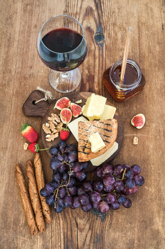Glass of red wine, cheese board, grapes,fig, strawberries, honey and bread sticks  on rustic wooden table
